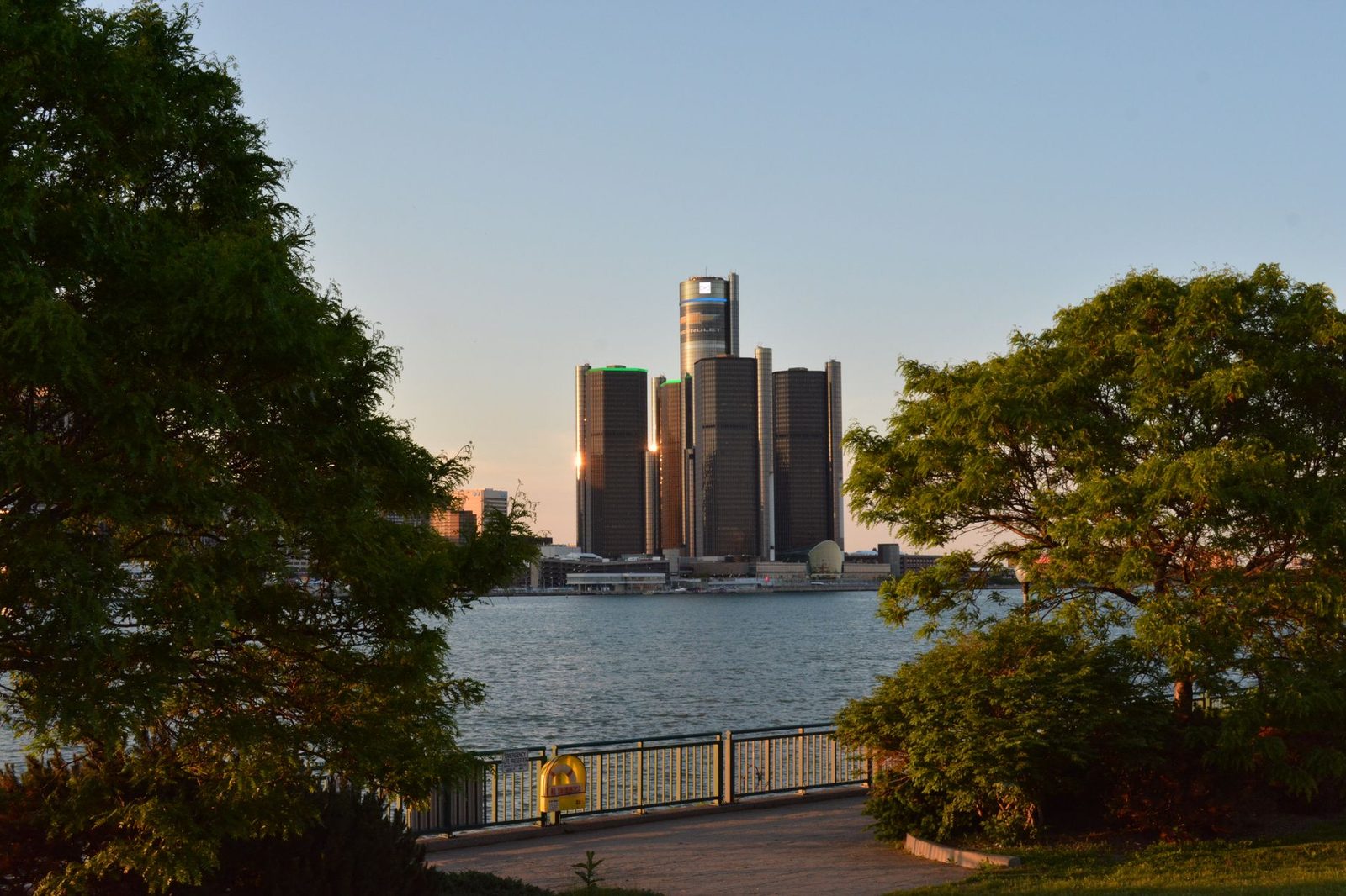 Scenic view of the Detroit Renaissance Center with lush trees framing the skyline at sunset.