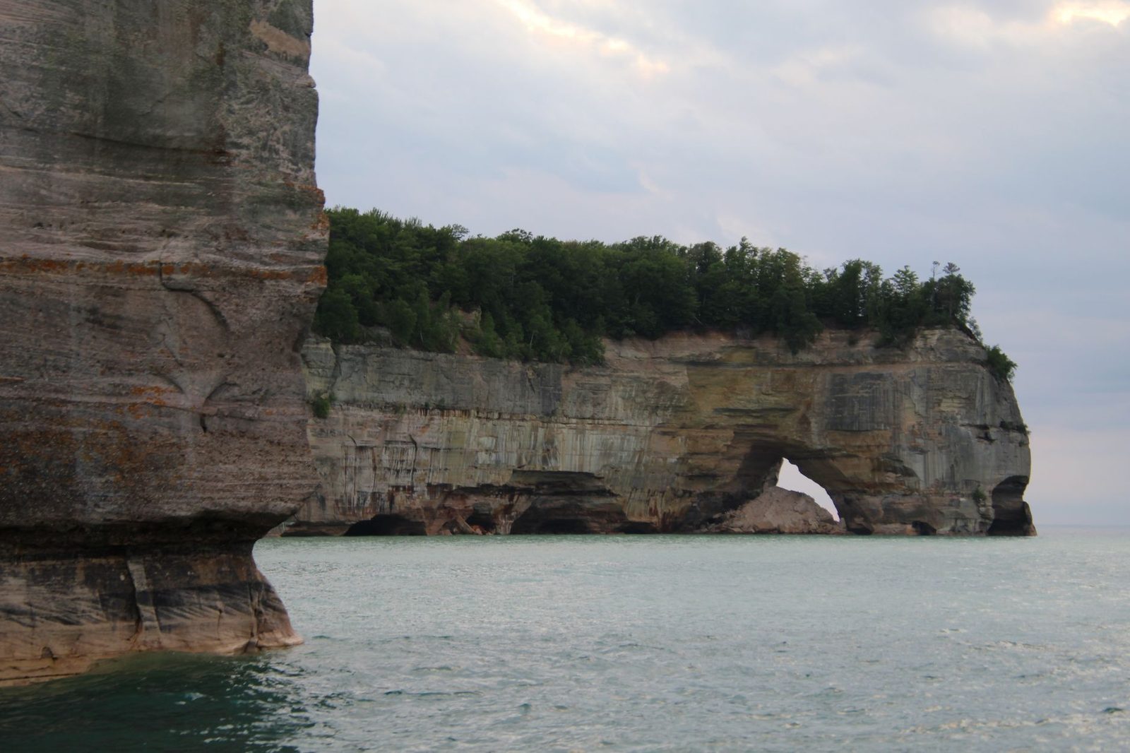 Dramatic limestone cliffs and arch at Pictured Rocks on a cloudy day.
